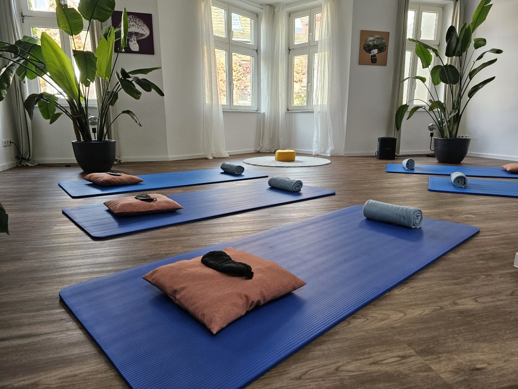 Blick in den Atemraum mit blauen Yogamatten, auf denen jeweils ein Kissen und eine Schlafmaske liegen