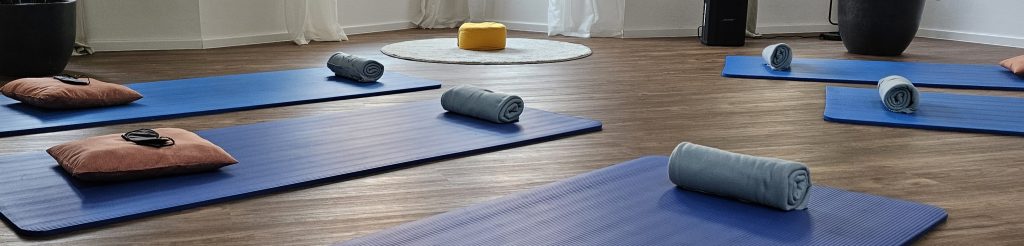 Blick in den Atemraum mit blauen Yogamatten, auf denen jeweils ein Kissen und eine Schlafmaske liegen