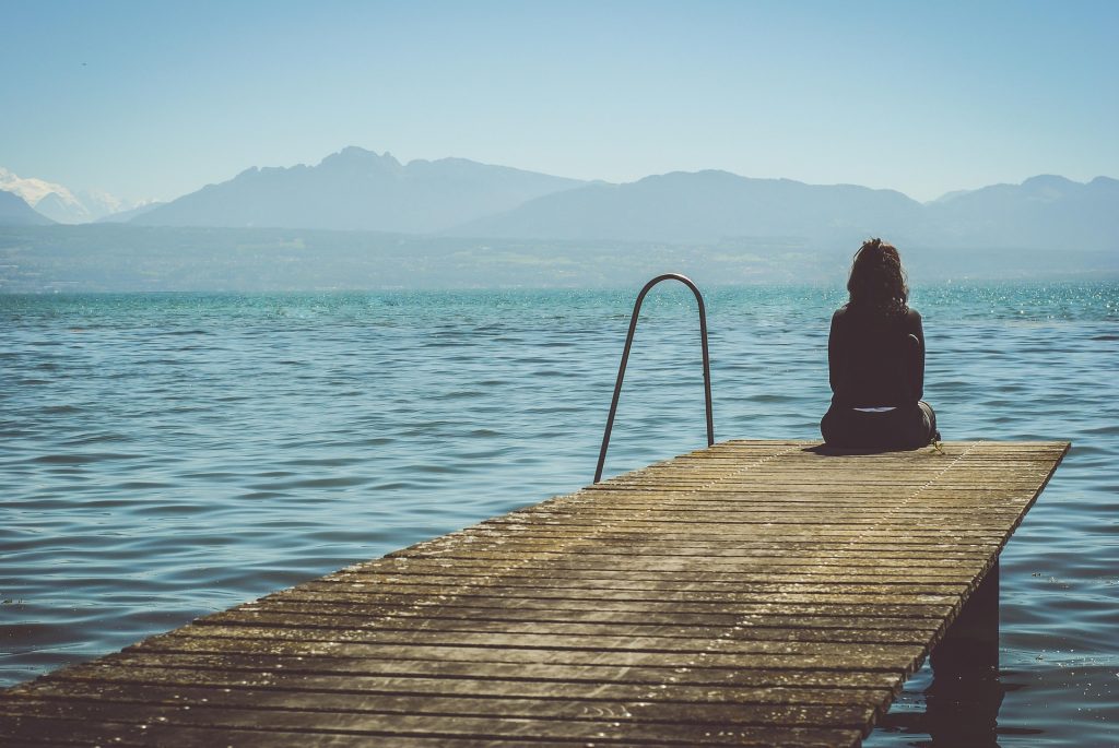 Eine Frau sitzt auf einem Steg und blickt auf einen See hinaus