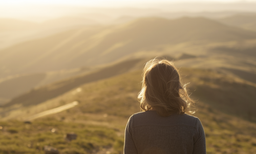 Eine Frau im Morgenlicht, die eine hüglelige Landschaft vor sich sieht